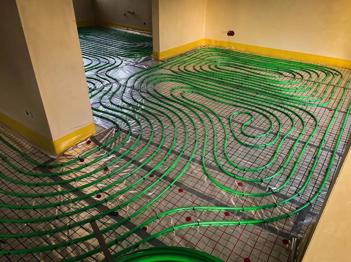 Zielone rury PEX ułożone ślimakiem na folii z siatką w nowym domu, gęsty rozstaw co 10 cm